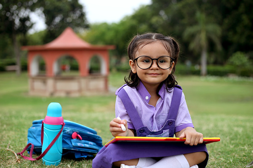 Small Indian schoolgirl studying in public park outdoors.