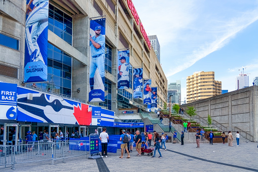 Toronto, Canada - May 13, 2023: Groups of people standing and walking outside the entrance of the Rogers Center. The building is adorned with banners featuring baseball players.