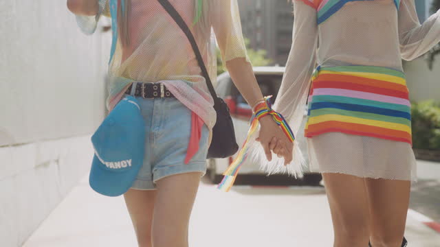 Close up of young asian transgender couple wearing rainbow dress couple holding hand and walking to Pride parade.
