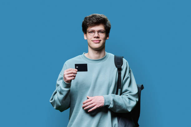 Young handsome guy student holding credit card in hands on grey background stock photo