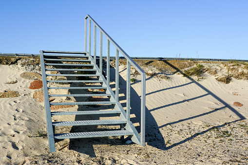 Public outdoor galvanized steel staircase with handrail for safety climbing on the embankment, blue sky background
