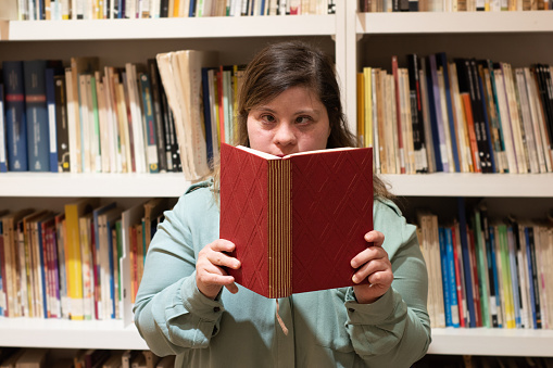 Portrait of a mid adult woman with special needs reading a book in the library