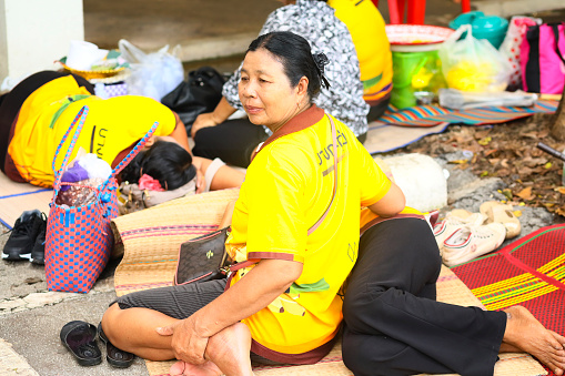 Portrait of relaxing and sleeping mature thai women at Public local traditional culture event organized by local government near historical grounds of Wat Wihan Thong Historical Site near Nan river and is local way of keeping history and traditions alive. Women are having a break on the grounds. One is sitting