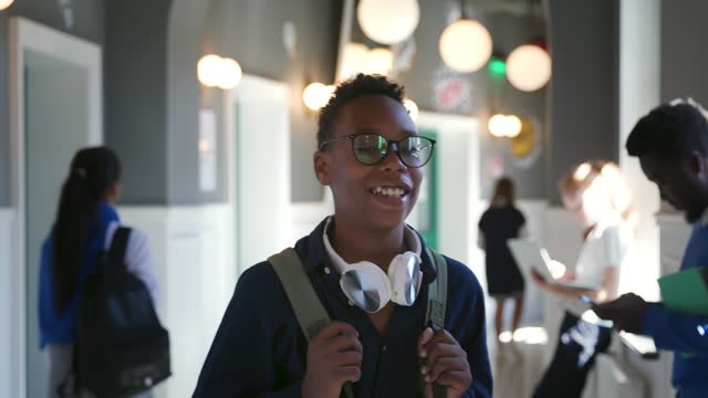 Smiling African-American schoolboy with backpack walk in campus corridor