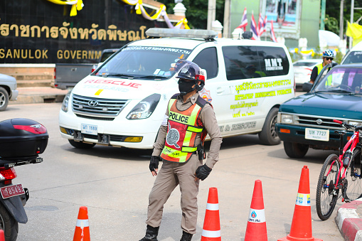 Thai traffic cop  standing in street of Phitsanulok. Cop is wearing helmet and is overviewing and securing the traffic and  street. Scene is around a local public health and cycling event for thai people organized by provincial government
