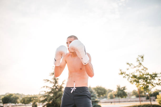 A young male kickboxer with boxing gloves trains in the park, outdoors