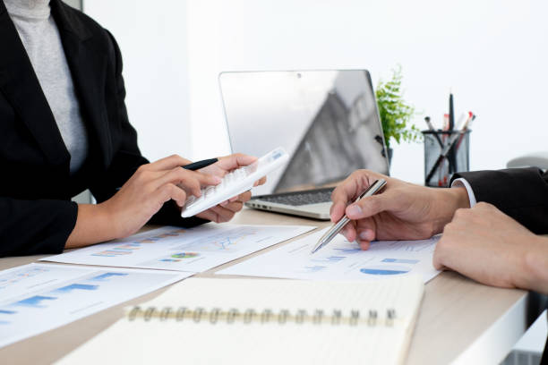 istock Two business people sitting at workplace and discussing about earnings on a graph to plan investments. 1496443872
