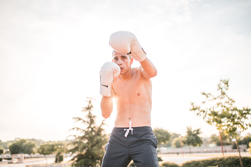 A young male kickboxer with boxing gloves trains in the park, outdoors