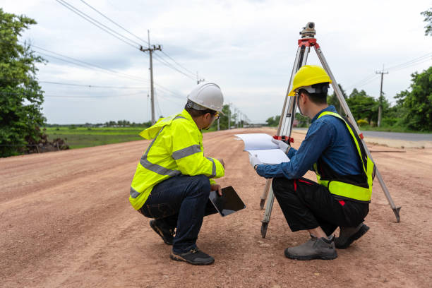 Asian engineer holding tablet to inspect work, with foreman using telescope to check pin against road plan, telescope and radio to control road construction, against road background under construction ingeniero asiático sosteniendo una tableta para inspeccionar el trabajo, con el capataz usando el telescopio para verificar el pasador contra el plan de carreteras, el telescopio y la radio para controlar la construcción de carreteras, contra el fondo de