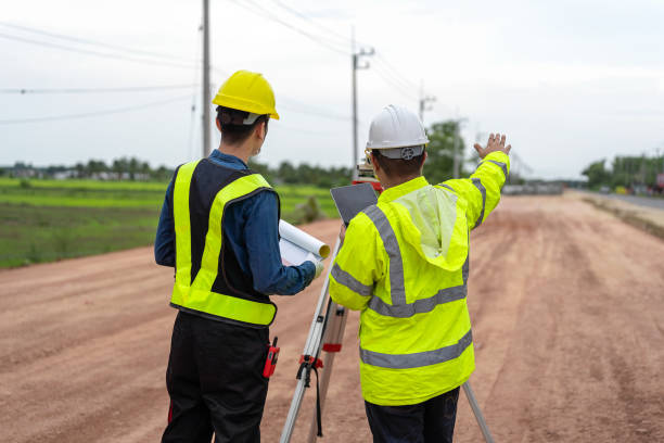 istock Asian engineer holding tablet to inspect work, with foreman using telescope to check pin against road plan, telescope and radio to control road construction, against road background under construction 1496447998