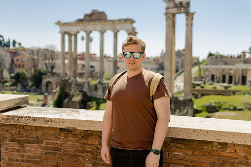Young man tourist resting at Roman Forum. Historical imperial Foro Romano from panoramic point of view, Italy