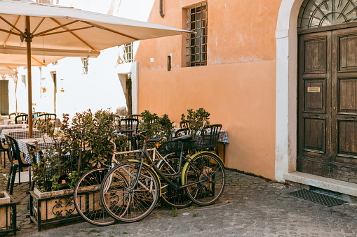 Bicycles parked on the street in Rome, Italy. Old bike against the orange wall at home. City transport concept. Lush green plants growing in pots near door of house