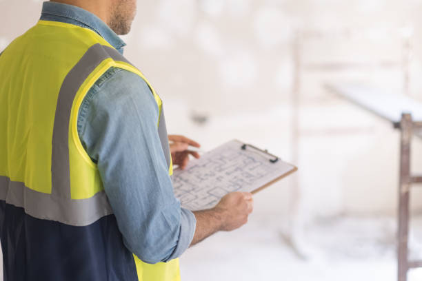 Foreman in vest checking drawing plan of big house holding clipboard in hands Foreman in vest checking drawing plan of big house holding clipboard and pen in hands man in professional uniform preparing for renovation process in room estate worker stock pictures, royalty-free photos & images