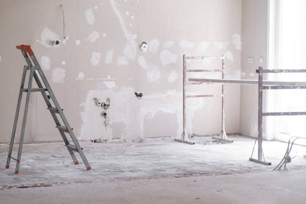 Ladder and construction equipment standing in empty room illuminated by bright sunlight shabby wall with holes and stains ready for painting renovation process in apartment