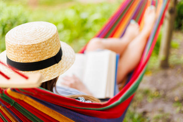 istock Young woman reading book while lying in comfortable hammock at green garden 1496457648