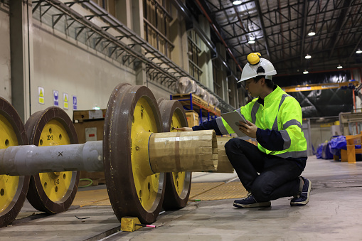 Asian railway engineer  mechanic wearing safety equipment (helmet and jacket) checking and inspecting the locomotive's powertrain. The core of train power system.