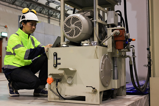 Young mechanical engineer with green safety jacket and white hardhat inspect hydraulic machine in factory,Asian railway engineer  mechanic wearing safety equipment (helmet and jacket) checking and inspecting the locomotive's powertrain. The core of train power system.