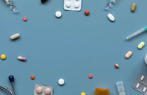 Top view of various pills and blisters and medical supplies on the blue background.