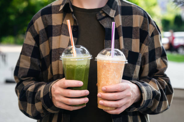 istock Man outdoors holding plastic cups with green and orange smoothies, close up. 1496460982