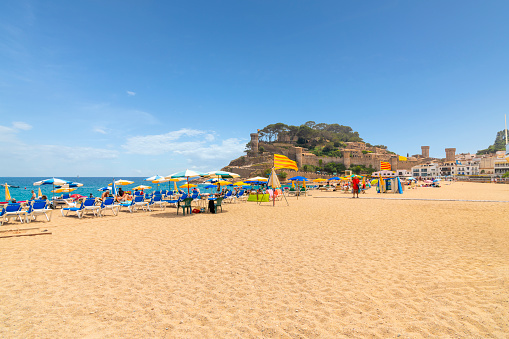 The picturesque sandy beach of Platja Glan along the Costa Brava coastline of the Mediterranean sea at the tourist resort town of Tossa de Mar, Spain. Spanish and tourists enjoy a sunny summer day at Platja Gran, the wide sandy beach at the Costa Brava town of Tossa de Mar with the 14th century Castle in view.