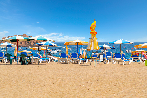 Beach chairs and colorful umbrellas along the sandy beach of Platja Glan along the Costa Brava coastline of the Mediterranean sea at the tourist resort town of Tossa de Mar, Spain.