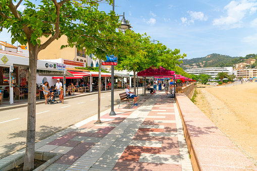 The pedestrian promenade of shops and cafes along the Platja Gran main beach at the seaside resort town of Tossa de Mar, Spain, along the Costa Brava coastline.