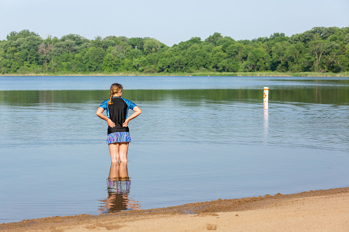 Rear view of a teenage girl standing in the shallow water at the lake on a summer day.