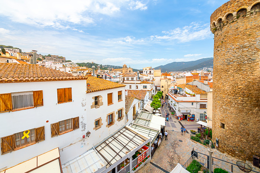 The whitewashed old town center filled with shops and cafes in the Spanish coastal town of Tossa de Mar, Spain, with the 14th century tower turret of the medieval castle in view on the Costa Brava coast.