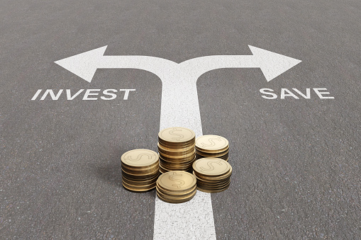 Stacks of gold coins on a traffic lane with split arrows pointing to left with the word INVEST and to the right with the word SAVE. Illustration of the concept of financial decisions