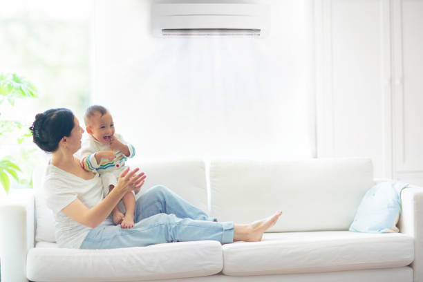 Mother and child with air conditioner remote Asian mother and child with air conditioner remote control. Comfortable temperature at family home. Cooling device. Mom and baby boy on couch under cold breeze. Air conditioning on hot summer day. air conditioner family stock pictures, royalty-free photos & images