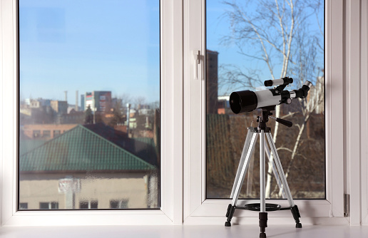 Tripod with modern telescope on windowsill indoors. Space for text