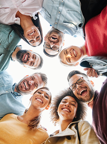 A multiethnic group of friends embrace and smile toward the camera. They're lined up loosely and desert vegetation, trees, and sagebrush are in the background.