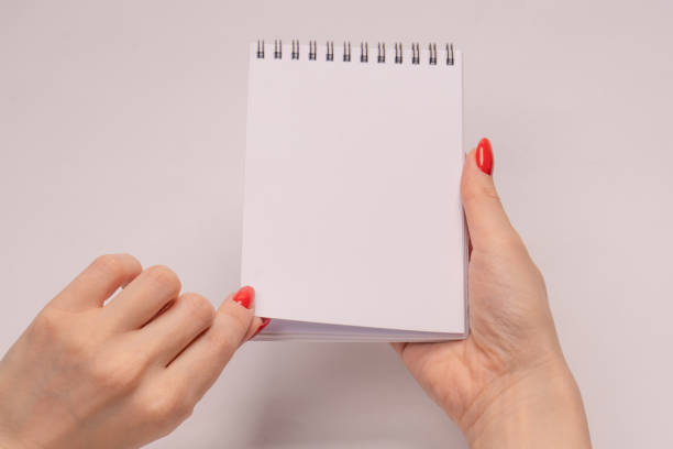 istock A notebook with empty white paper in woman hands with red nails. 1496466737