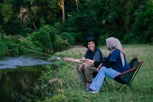 Asian couple doing outdoor activity by fishing together at the river. People enjoying nature.