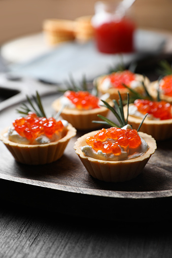 Delicious tartlets with red caviar and cream cheese served on wooden table, closeup