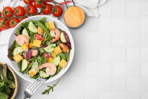 istock Delicious salad with croutons, cucumber and shrimp served on white tiled table, flat lay. Space for text 1496471289