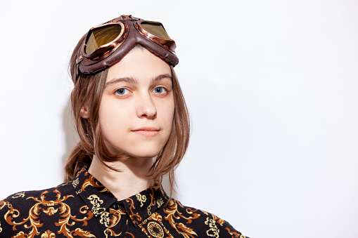 Close-up studio portrait of an attractive young white woman with brown hair with motorcycle goggles against a white background
