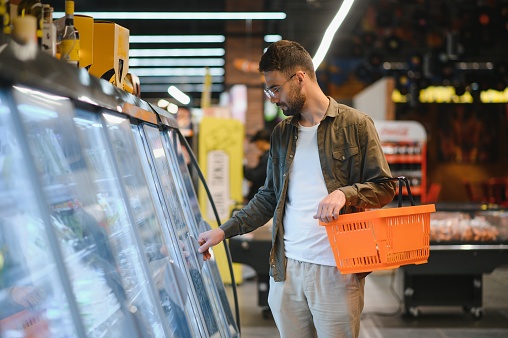 Portrait of smiling handsome man grocery shopping in supermarket, choosing food products from shelf.