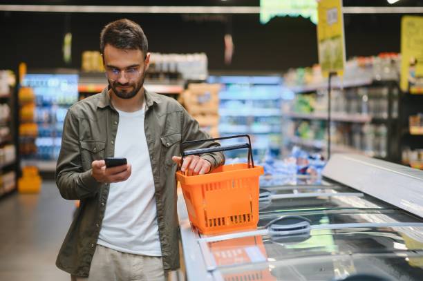 istock Handsome man shopping in supermarket, smilling, using phone. 1496473016