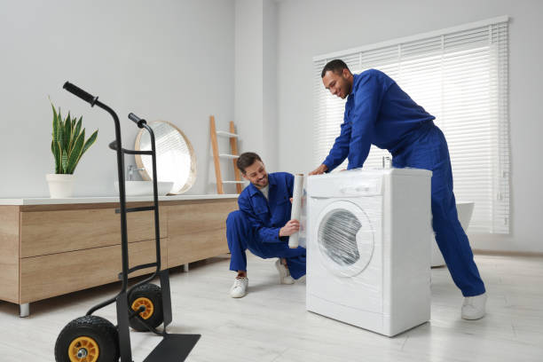 Male movers with stretch film wrapping washing machine in bathroom. New house