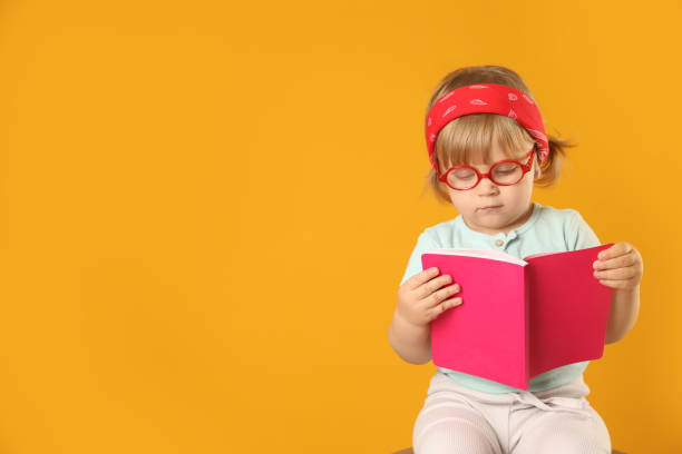 istock Cute little girl in glasses with notebook on orange background. Space for text 1496473572