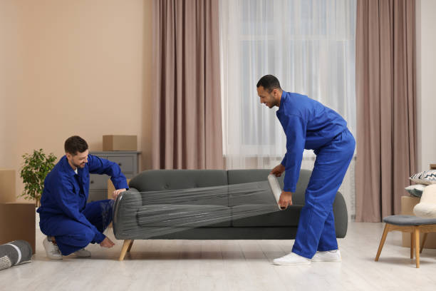 Male movers with stretch film wrapping sofa in new house