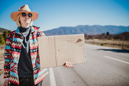 istock Woman hitchhiking alone and holding empty cardboard sign 1496481439