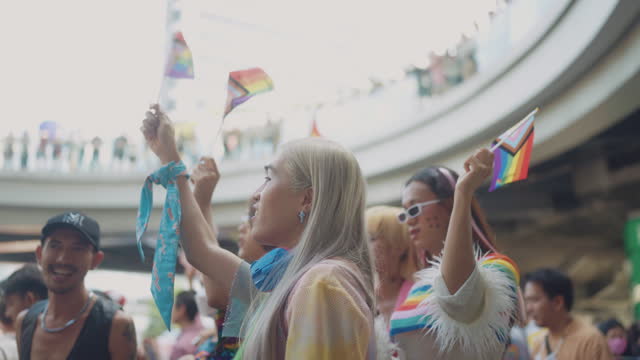 During a pride parade asian group of LGBTQ+ is happy to participate against a background of people waving rainbow flags.