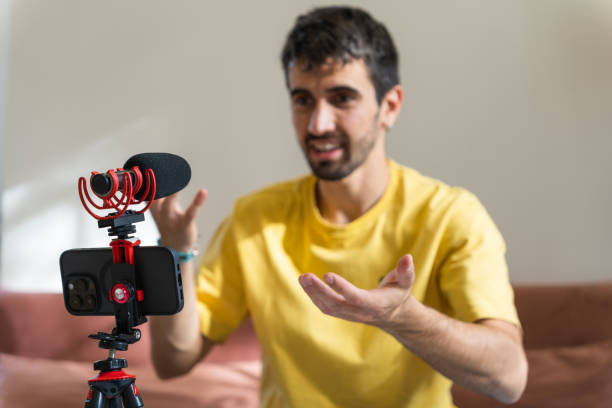 istock Blogger filming video with smart phone on tripod and microphone for vlog. Content creator using mobile phone, tripod and microphone to record for social media. Young man giving explanations trough a video call using his mobile phone and a microphone 1496488370