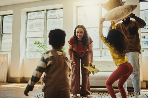 A family of four is having a pillow fight in an open and airy living room space at home while smiling and laughing. Copy Space. Stock Photo