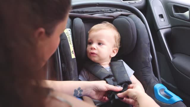 Mother Fastening The Seat Belt Of A Child Car Seat