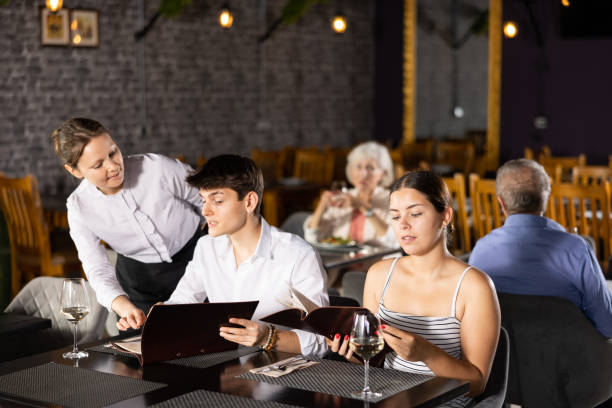 istock Young couple discussing menu with waitress at table in restaurant 1496496007
