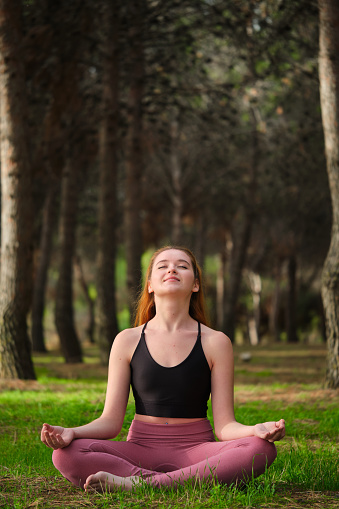 Redhead young woman meditating in a forest. Meditation in nature.