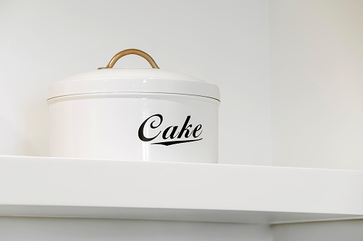 Beautiful white vintage kitchenware. Cake Tin with Cover Lid and Round Handle. walls are white color, very clean place, lightning is perfect